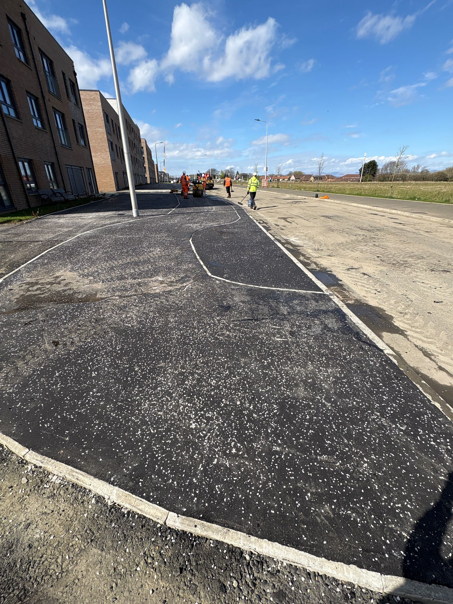 Footway in final finishing stage with operatives ensuring consistent surface quality and compaction
