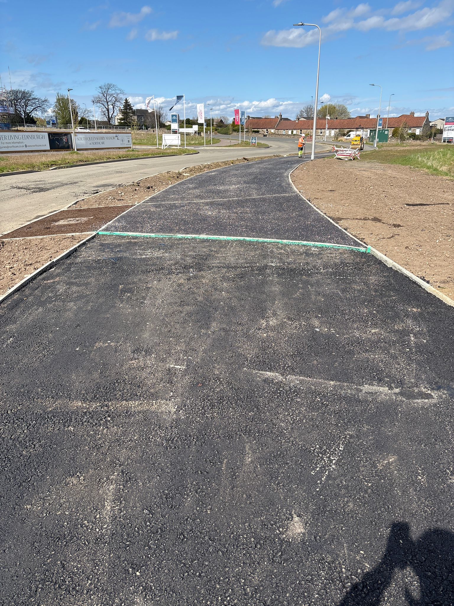 Completed footpath with smooth asphalt finish and clean kerb lines following the road layout